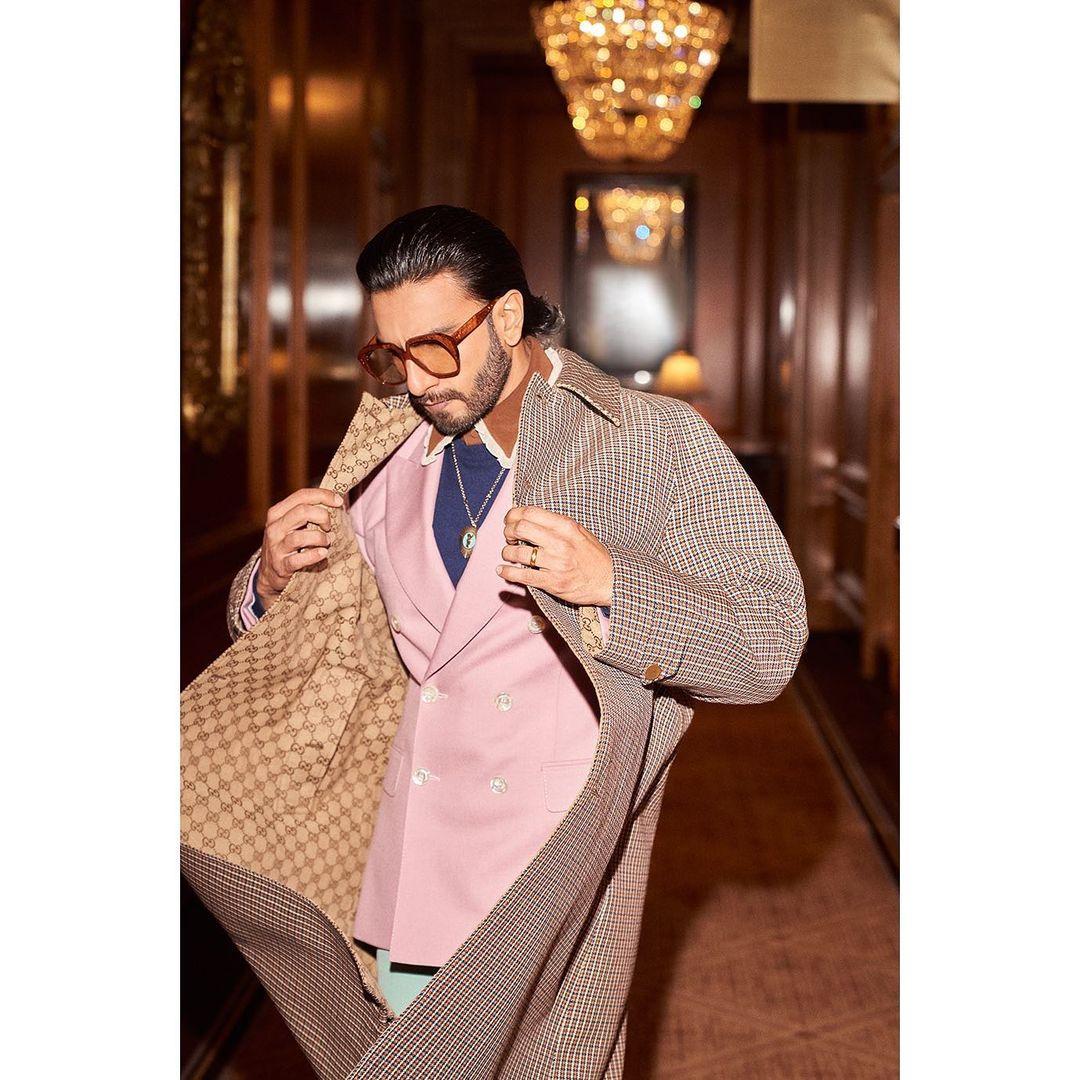Layering is the name of the game as he effortlessly combines a brown shirt, a navy blue sweater, and a pink suit jacket.